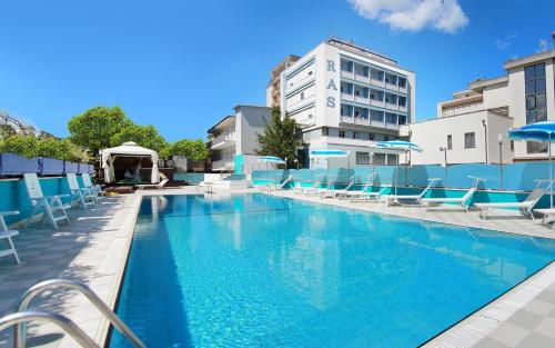une piscine avec des chaises bleues et un bâtiment dans l'établissement Hotel Ras, à Gatteo a Mare