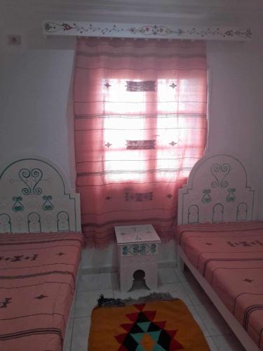 a room with two beds and a window with pink curtains at Appartement yakine in Midoun