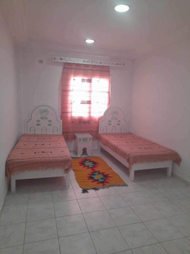 two beds in a room with a window and a rug at Appartement yakine in Midoun