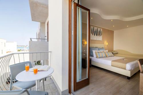 a bedroom with a bed and a balcony with a table at Hotel Soffio D'Estate in San Vito lo Capo