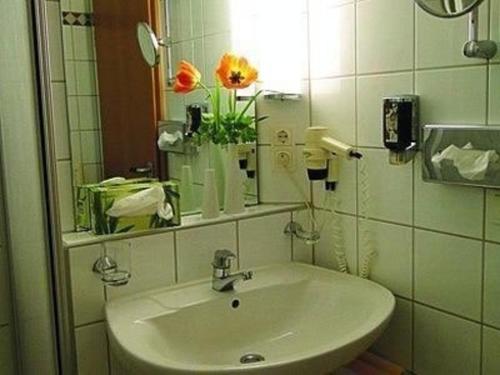a bathroom with a sink and a mirror and flowers at Apartment Bayrischer Wald am Golfclub im Feriendorf Glasgarten in Rötz