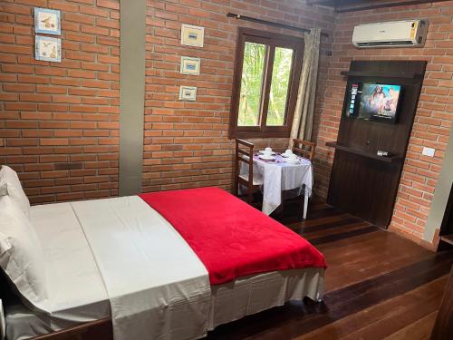 a bedroom with a bed with a red blanket and a table at Pousada Nosso Bosque in Porto Belo