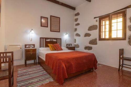 a bedroom with a bed with a orange blanket and a window at El Zumacal in Valleseco