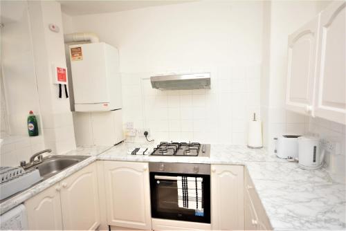 a white kitchen with a stove and a sink at Lovely 3 Bedroom Apartment in Standford Hill in London