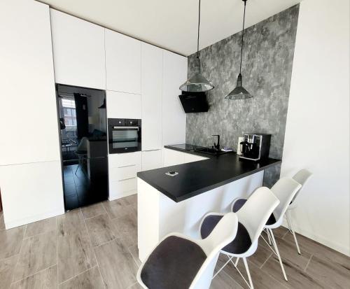 una cocina con armarios blancos y una encimera y sillas negras. en Apartament nad Jeziorem en Olecko
