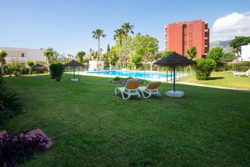 twee stoelen en parasols in een tuin met een zwembad bij Estudio bajo con piscina in Torremolinos