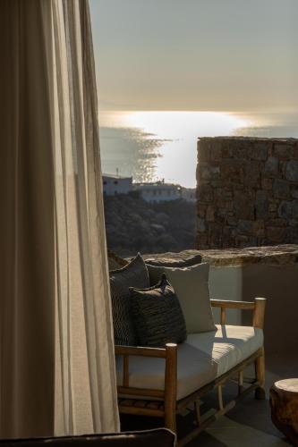 a bench with pillows on a balcony with the ocean at Nomia Sunset Suites Mykonos in Tagou