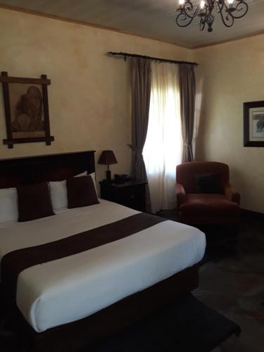 a bedroom with a bed and a chair and a window at The Big Five Lodge in Gaborone