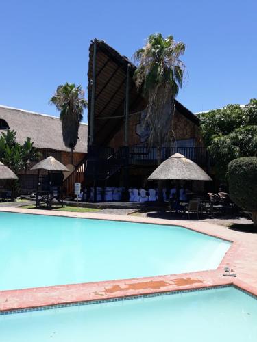 a swimming pool in front of a building with palm trees at The Big Five Lodge in Gaborone