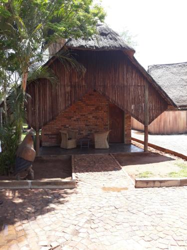 a building with a straw roof with chairs and a tree at The Big Five Lodge in Gaborone
