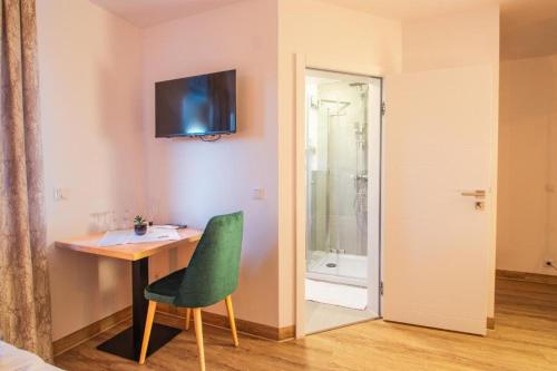 Habitación con escritorio, silla verde y ducha. en Hotel Dona en Bergisch Gladbach