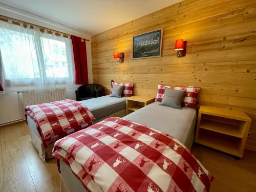 two beds in a room with wooden walls at Hôtel Chalet Le Panoramique in Mizoën