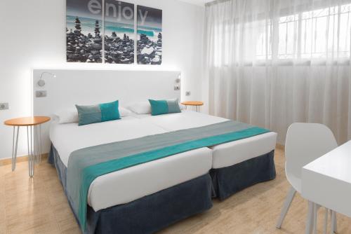 a white bedroom with a large bed with blue pillows at Saint George in Los Cristianos