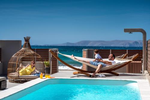 a group of people sitting in a hammock next to a pool at Anasa Luxury Villas with Heatable Pool in Kokkini Khanion