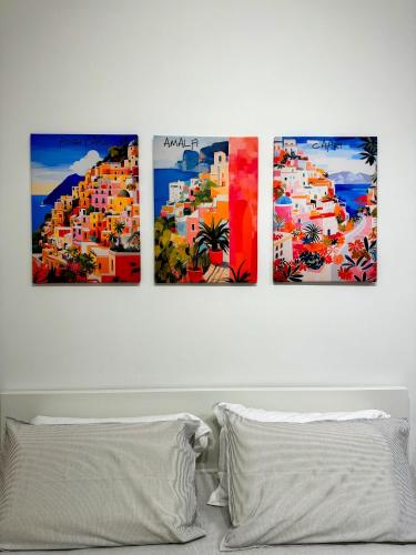four paintings on a wall above a bed at EllePì Rooms in Naples