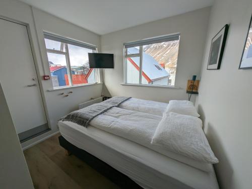 a white bedroom with a bed and two windows at The Ísafjörður Inn in Ísafjörður