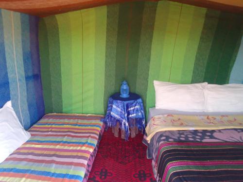 a room with two beds and a side table at Camp Familia Erg Chebbi in Merzouga