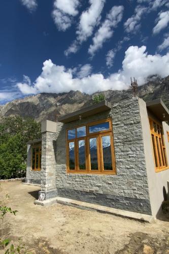 una pequeña casa con ventanas y montañas en el fondo en Home of golden oriole, en Hunza