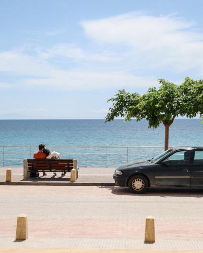 two people sitting on a bench looking at the ocean at Aegean Blue Beach Hotel in Nea Kalikratia