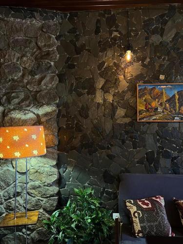 a room with a stone wall with a couch and a lamp at Guest House Nikala in Mestia