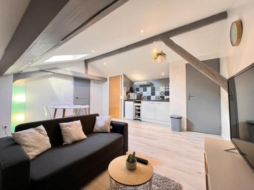 un salon avec un canapé noir et une cuisine dans l'établissement LE CLOS CHASSAING N5-WiFI-CENTRE VILLE-CLIMATISATION, à Périgueux