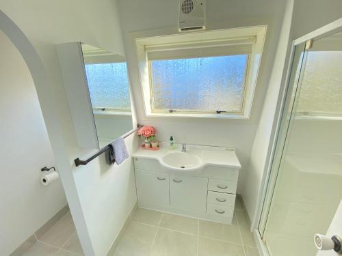 a white bathroom with a sink and a window at Coastal Charm in Patons Rock in Rangihaeata