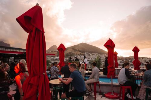 un grupo de personas sentadas en mesas con sombrillas rojas en Radisson RED Hotel V&A Waterfront Cape Town en Ciudad del Cabo