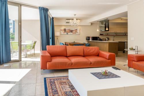 a living room with an orange couch and a kitchen at V&A Waterfront Luxury Apartments by McStay in Cape Town