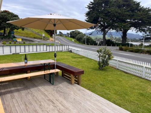 a picnic table with an umbrella on a deck at Kopu Cottage - in the heart of Raglan. in Raglan