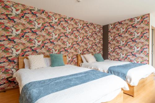 two beds in a room with a floral wallpaper at 梅田まで電車で5分 1フロア貸切 駅徒歩3分 2024年フルリフォーム 建物2階 in Osaka