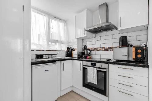 cocina blanca con armarios blancos y ventana en Pass the Keys Modern Flat near Tower Bridge en Londres