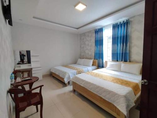 a hotel room with two beds and a table and a desk at Nhà nghỉ Kim Cương in Rach Gia
