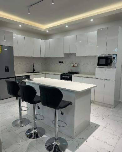 a kitchen with white cabinets and a counter with stools at REOs Smart Haven with Pool in Oblogo