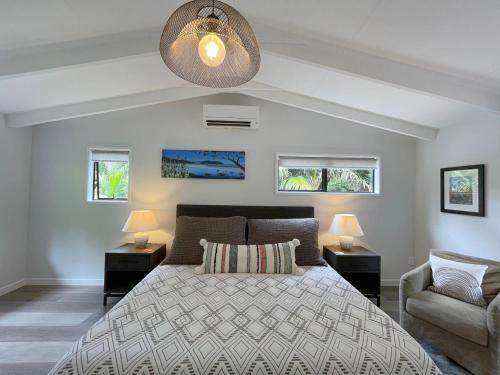 a bedroom with a bed and two lamps and a chair at Tui Cottage - Waiheke Escapes in Onetangi