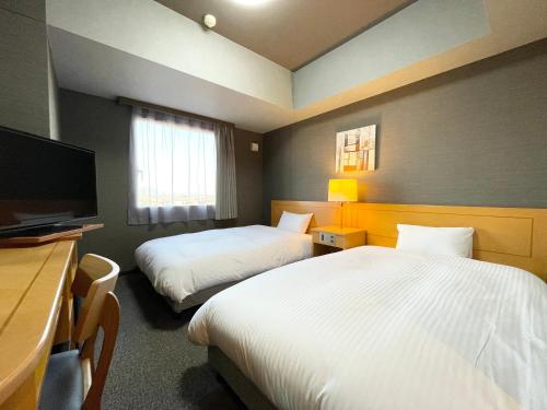 Habitación de hotel con 2 camas, escritorio y TV. en Hotel Route-Inn Yuki, en Yuki