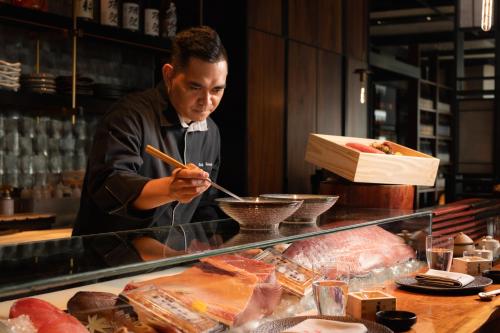 a man cooking food in a restaurant with chopsticks at Rosewood Phnom Penh in Phnom Penh