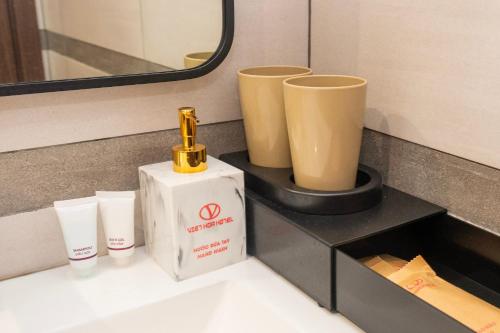 a bathroom counter with a bottle and two cups at Cat Ba Viet Hoa Hotel & Residence - Pool & Bar in Cat Ba