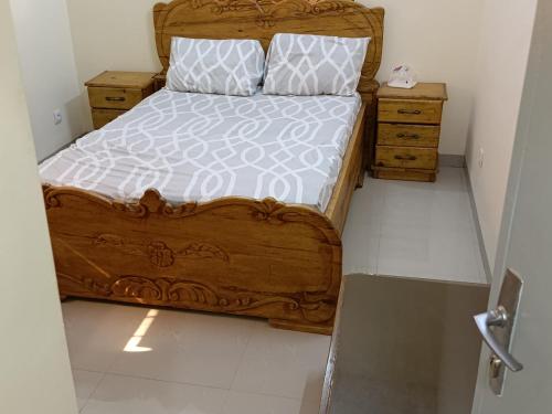 - une chambre dotée d'un lit en bois avec des draps et des oreillers blancs dans l'établissement Résidence lynda prestige Ouaga 2000, à Ouagadougou