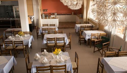 コモティニにあるVosporos Hotelの白いテーブルと椅子(花付)が備わるレストラン