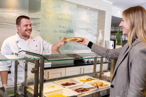 a woman is handing a man a plate of food at Hotel Regina Maris in Norddeich