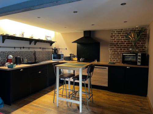 une cuisine avec des placards noirs et une table avec des tabourets dans l'établissement Maison la clé du soi, à Duclair