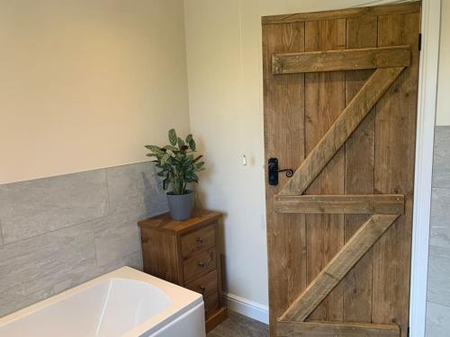 a bathroom with a wooden door next to a bath tub at Woodside Retreat with Luxury Hot Tub in Retford