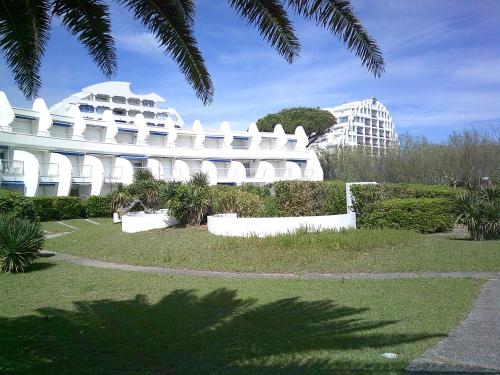 un edificio blanco con árboles y plantas delante de él en Vittoria Immobilier-375-Vue mer- REGLEMENT SUR PLACE -Chèques Vacances acceptés, en La Grande-Motte