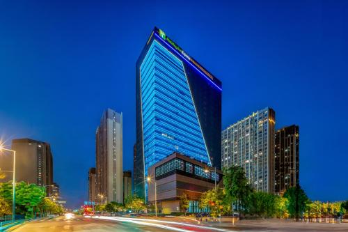 un edificio alto de cristal en una ciudad por la noche en Holiday Inn Express Nanjing Riverside, an IHG Hotel en Nankín