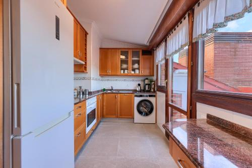 a kitchen with wooden cabinets and a white refrigerator at Ático con 2 terrazas, 25m2 cada una By urban hosts in Górliz-Elexalde