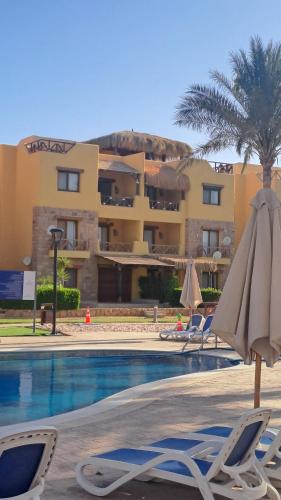a hotel with a swimming pool with chairs and an umbrella at Luxury Chalet in Mountain View 2 , El-Sokhna with Sea View , Pool View "Heated Pool" and Garden View Families Only in Ain Sokhna