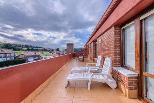 a balcony with white chairs on a brick building at Atico con 2 terrazas de 25 m cada una in Górliz-Elexalde