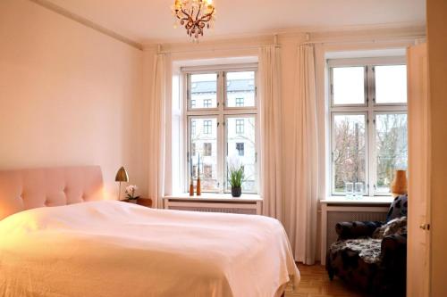 um quarto com uma cama branca e 2 janelas em Serviced Luxury Apartment in Østerbro - incl housekeeping once a week em Copenhague