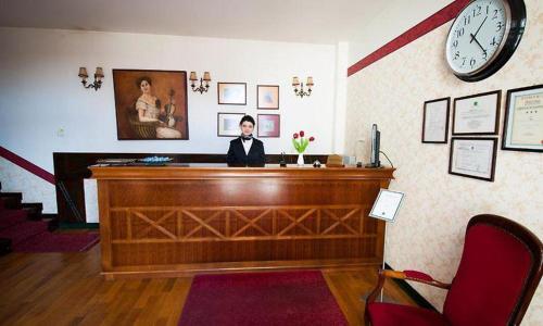 a woman sitting at a desk in a room with a clock at Hotel Ana in Arad