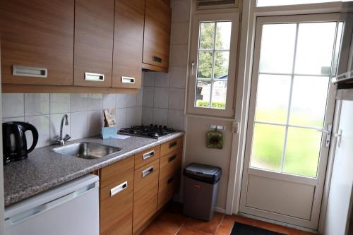a kitchen with wooden cabinets and a sink and a window at 2-person bungalow Heuveltjes in Voorthuizen